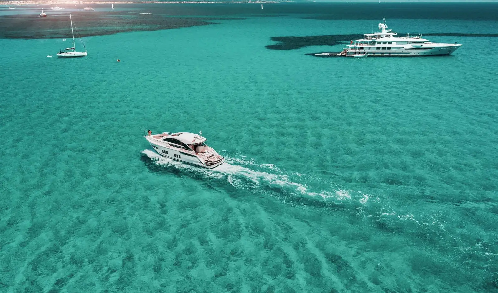 Luxury motor yacht cruising across clear emerald waters along the coast of Capeside Marina Residences Sobha Siniya Island.