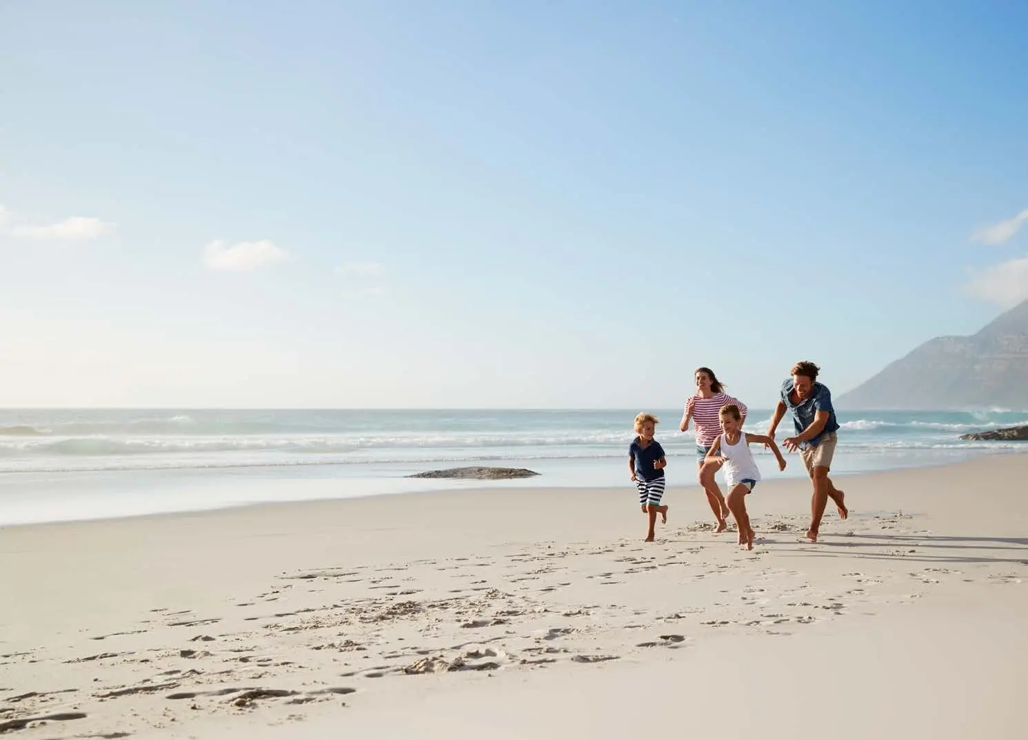 Happy family enjoying coastal lifestyle walks along white sand beach near Pearlside Marina Residences Sobha Siniya Island.