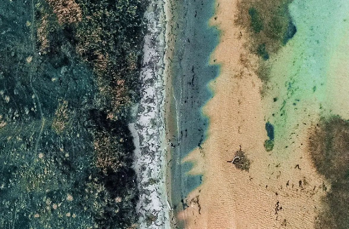 Pristine aerial view of natural shoreline and turquoise shallow waters framing the coastal community of Pearlside Marina Residences in Umm Al Quwain