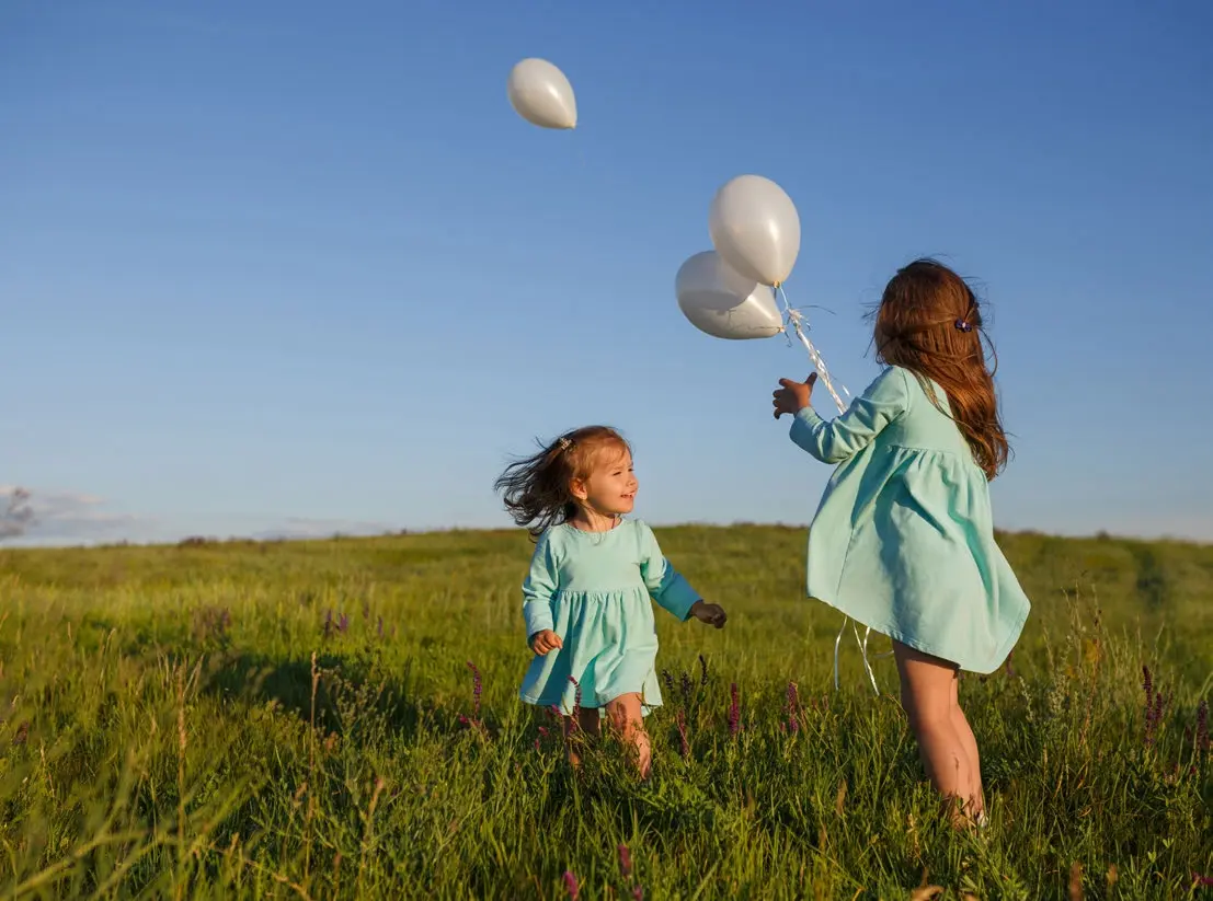 Two little girls playing with white balloons on a green field at Bayside Marina Residences on Sobha Siniya Island